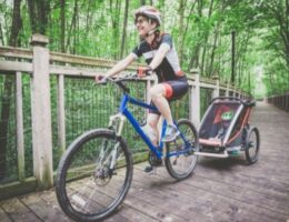 Cyklist med hjälm drar en barnsitsliknande cykelkärra på skogsstig
