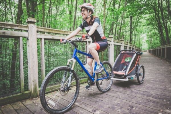Cyklist med hjälm drar en barnsitsliknande cykelkärra på skogsstig
