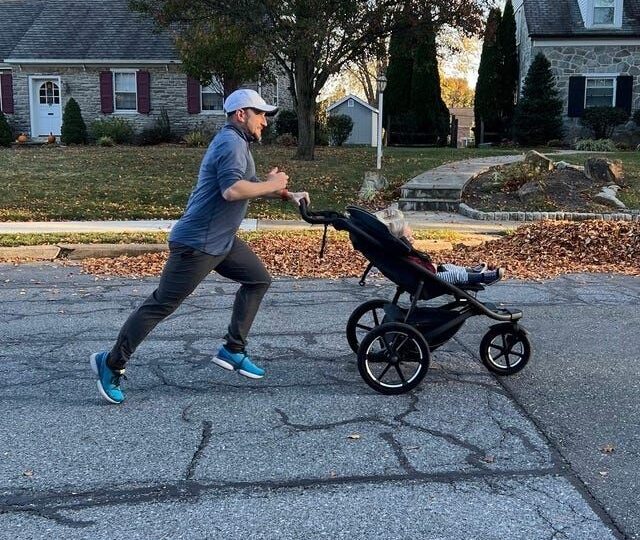 Löpare skjuter en joggingvagn framför sig på en villagata