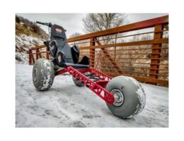 Röd fyrhjulig vagn med snötäckta däck på en isig bro