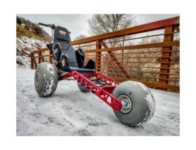 Röd fyrhjulig vagn med snötäckta däck på en isig bro