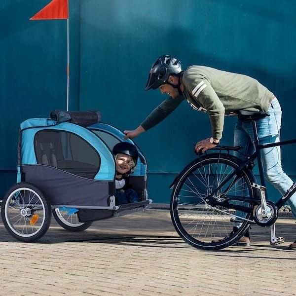 Vuxen cyklar med hjälm bredvid en cykelkärra med hjälmburet barn