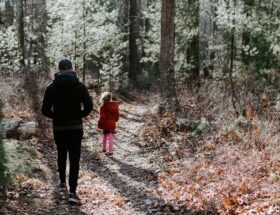 Vuxen och litet barn vandrar på en skogsstig i kuperad terräng